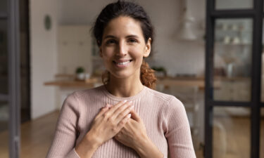 Head shot portrait smiling woman folded hands on chest, feeling self-compassion