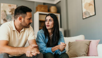 man wearing yellow shirt and woman wearing blue top sitting on the couch together being vulnerable with each other during a conversation about benefits of vulnerability