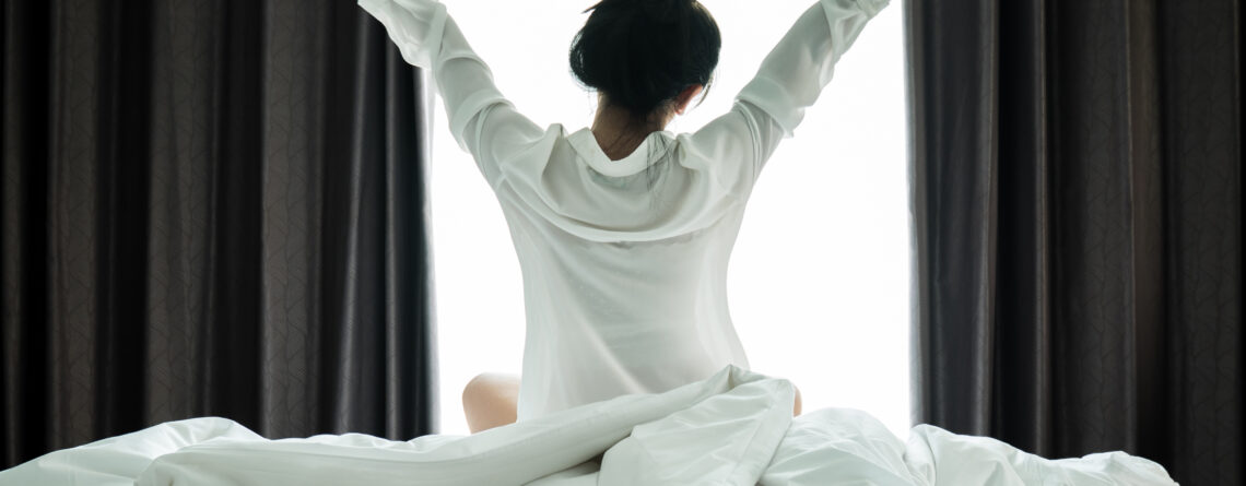 Asian women wake up from sleep. She stretches herself in the morning on the weekend sit on the bed, Relax and weekend concept to have the best morning routine