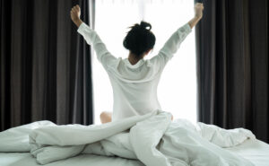 Asian women wake up from sleep. She stretches herself in the morning on the weekend sit on the bed, Relax and weekend concept to have the best morning routine