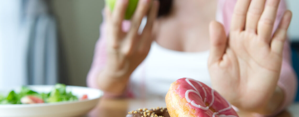 Young girl rejecting junk food or unhealthy food such as donuts and choosing to eat an apple instead displaying attributes of having an obsession with eating healthy