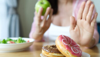 Young girl rejecting junk food or unhealthy food such as donuts and choosing to eat an apple instead displaying attributes of having an obsession with eating healthy